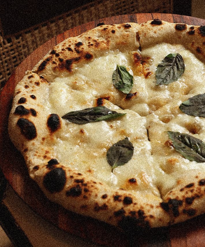 A wood-fired pizza being finished by hand at Amichi
